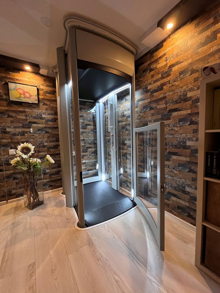 Senkrechtlift myHomelift in einer Ecke eines Wohnraumes mit geöffneter Tür