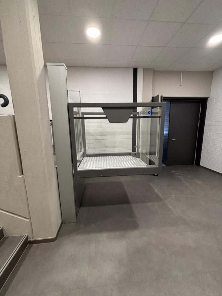 Plattformlift von oben gesehen, mit Glasgeländern und Metallboden im Bereich eines Flurs.