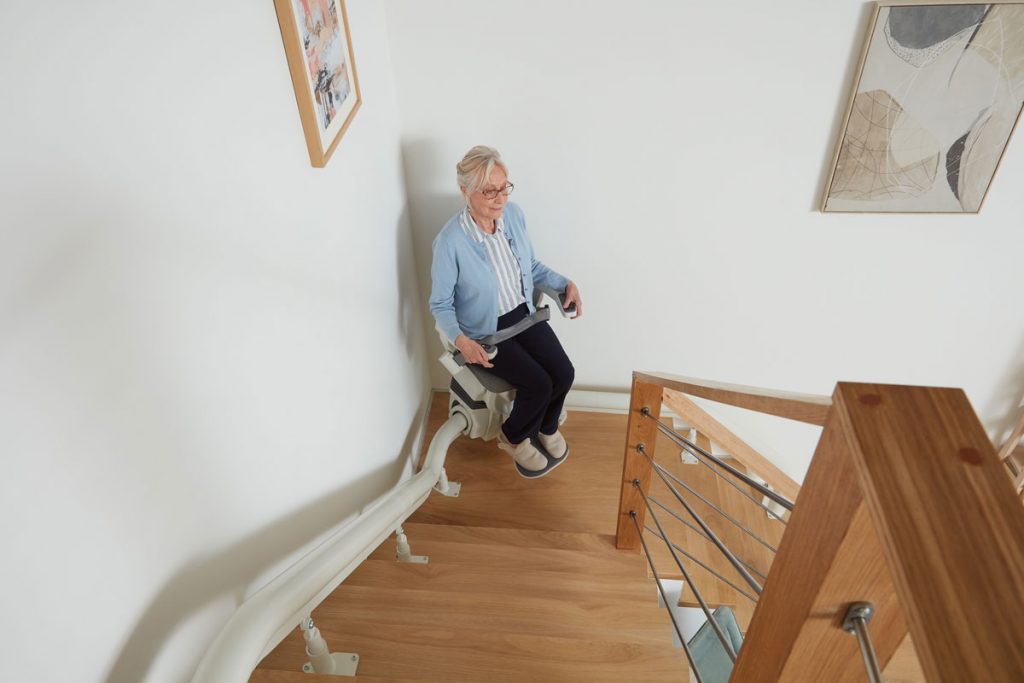 Eine ältere Frau, die mit einem Ultimate Treppenlift die Treppe hoch fährt.