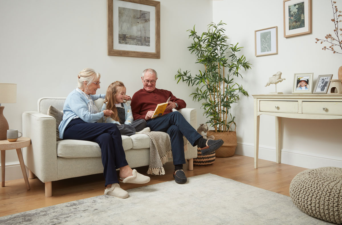 Großvater und Großmutter sitzen mit ihrem Enkelkind auf dem Sofa und lesen gemeinsam in einem Buch.
